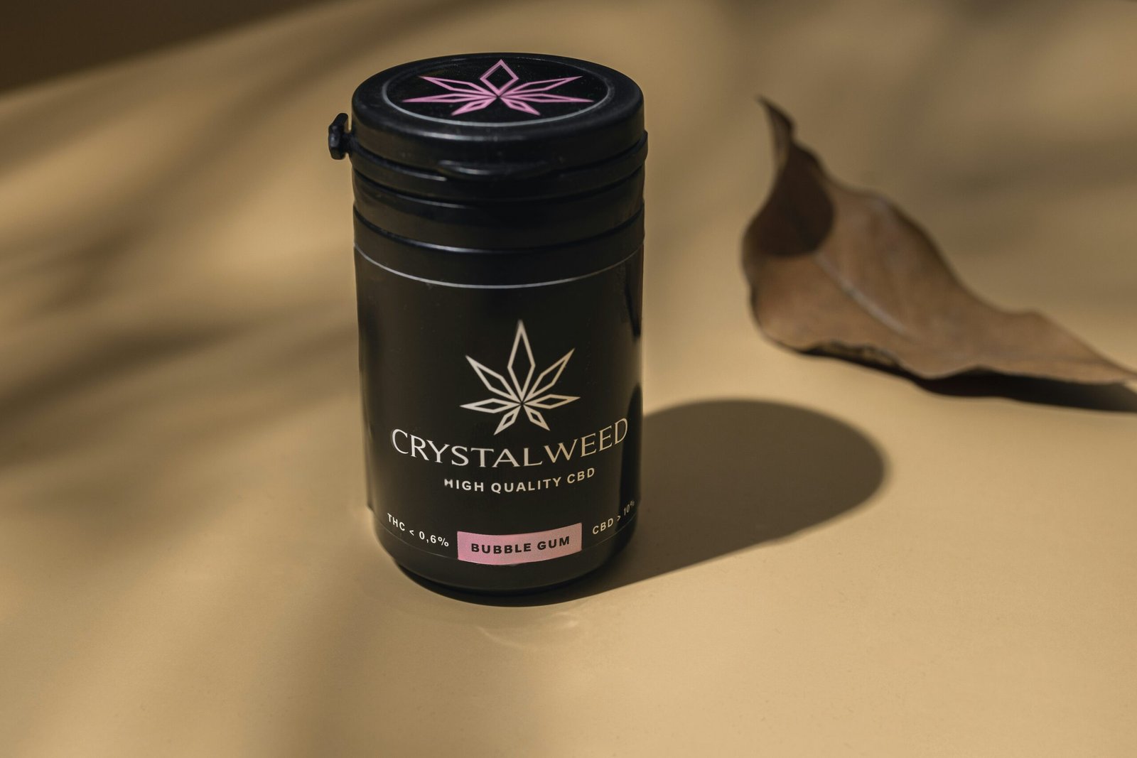 a black container with a pink flower on it next to a leaf