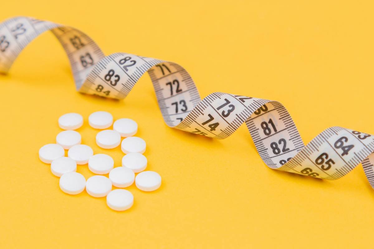 White measuring tape with a white pills, white vitamin on a yellow background. Diet. Slimming. Obesity. Place for an inscription. Weight loss marathon. Advertising. Top view. The close plan.